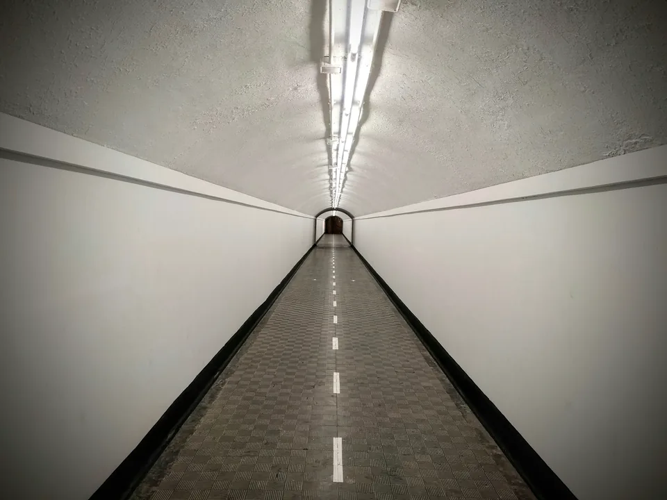 Túnel blanco con una pasarela oscura y luces alineadas hacia el fondo