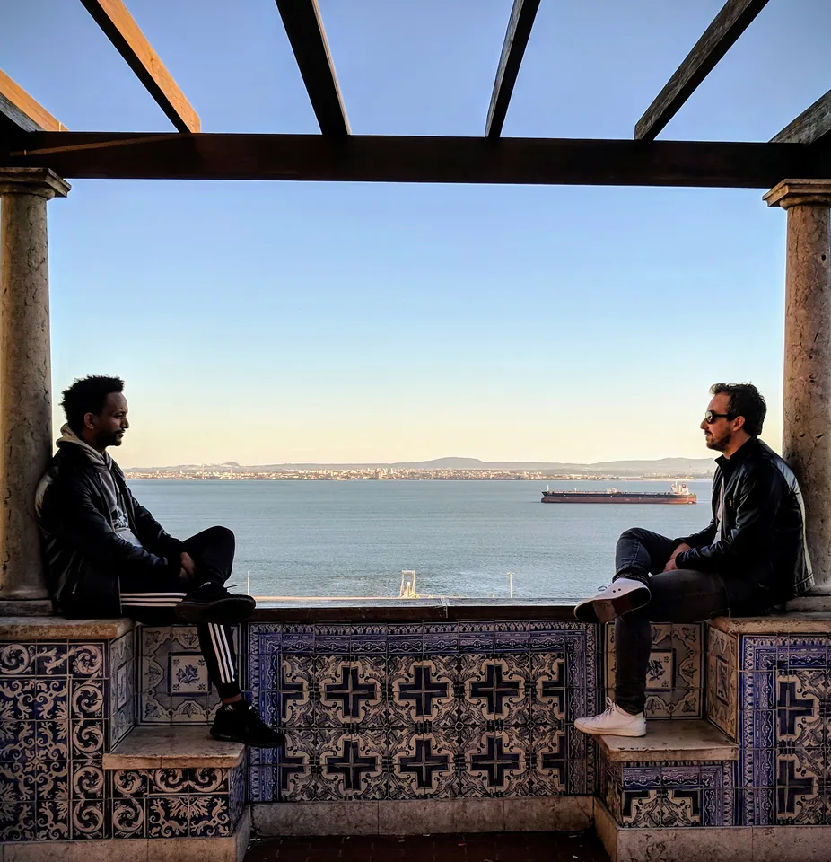 Dos personas sentadas frente al agua bajo una estructura de madera