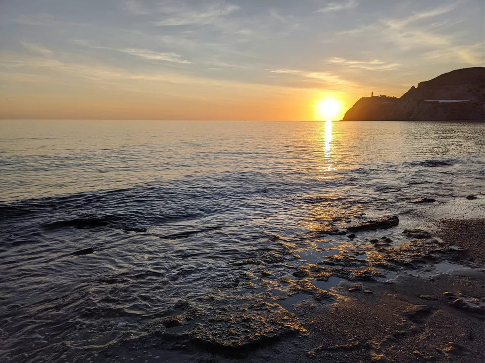 Sol cerca del horizonte sobre el mar y una playa de guijarros
