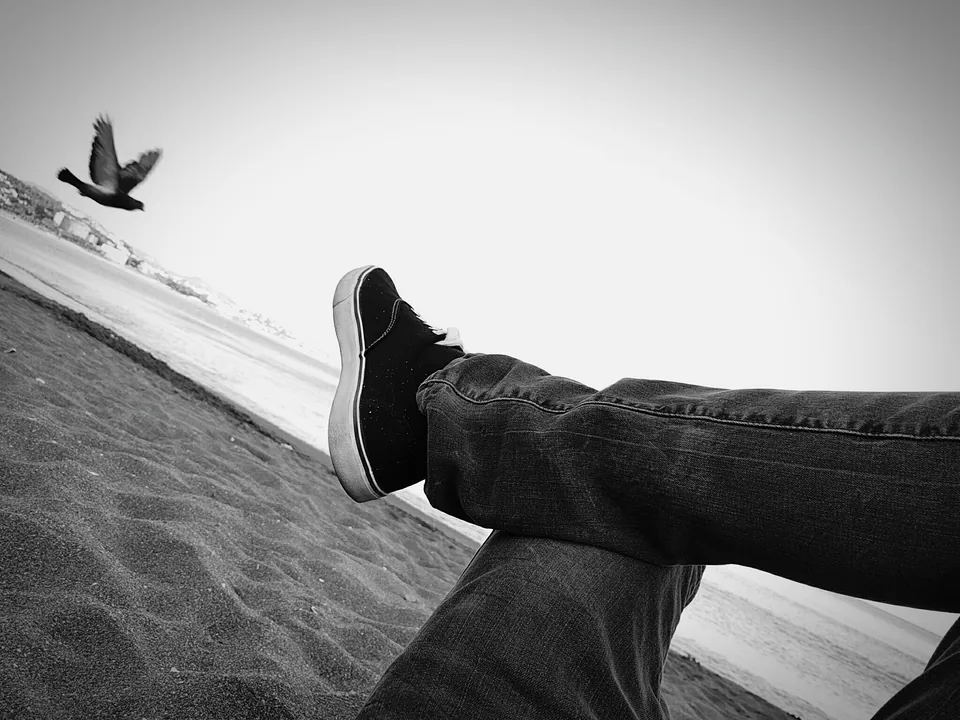 Piernas apoyadas en un muro junto a una paloma, en blanco y negro
