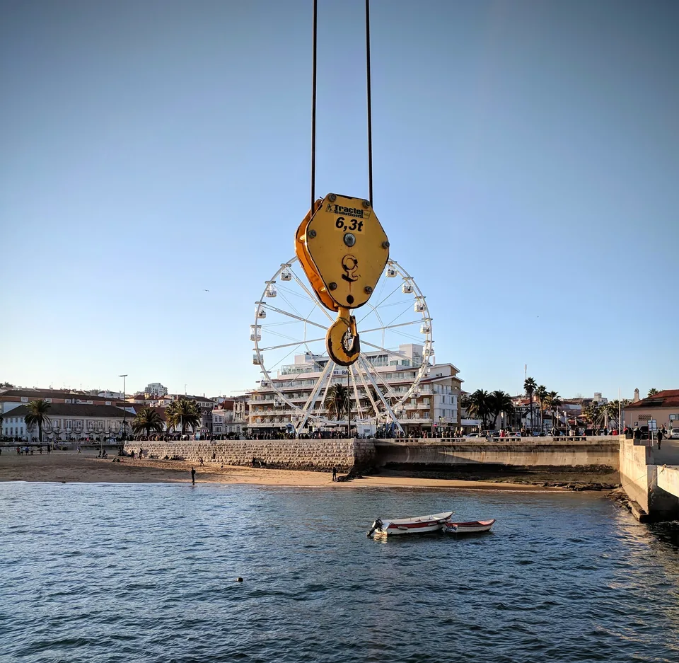Polea amarilla suspendida junto al río y una noria al fondo