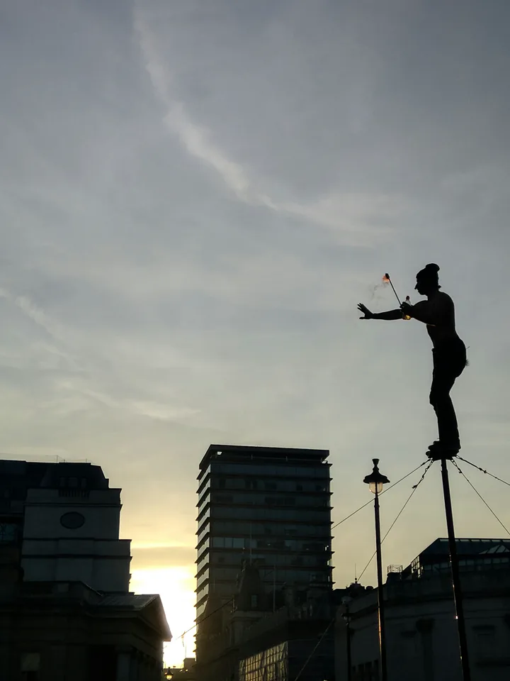 Escultura de una figura elevada sobre un poste bajo nubes grises