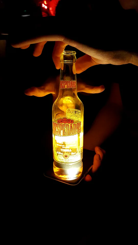 Botella iluminada sostenida en la oscuridad