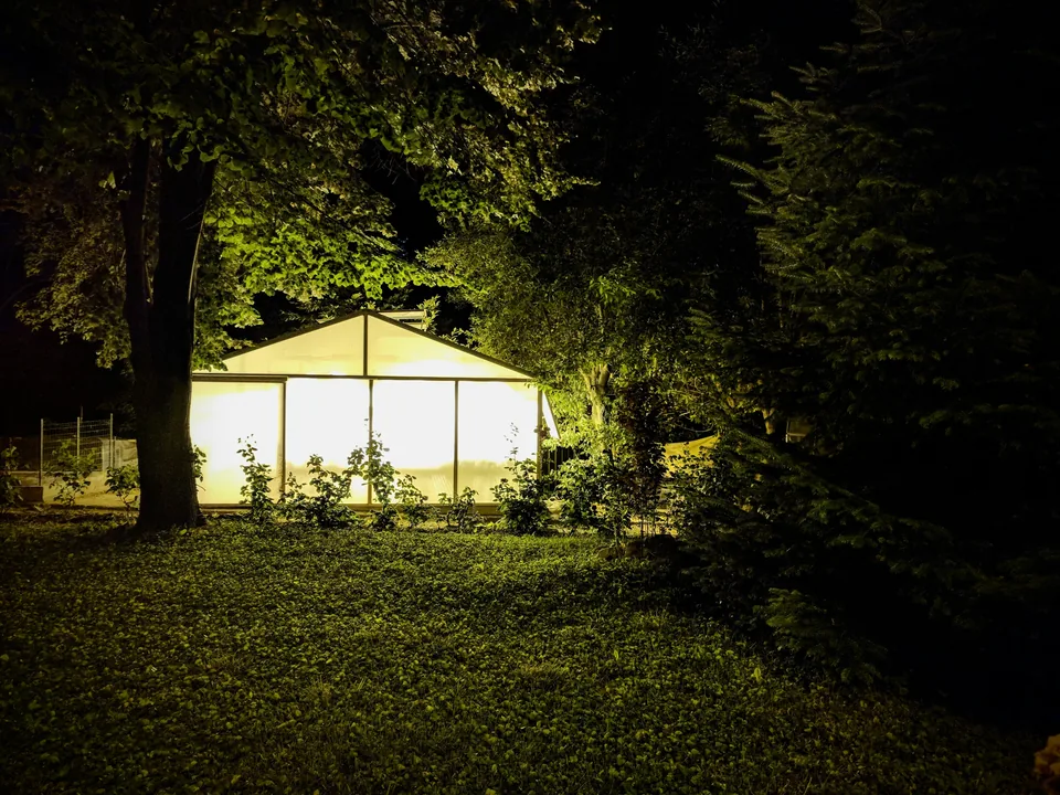Invernadero iluminado de noche en un jardín rodeado de árboles